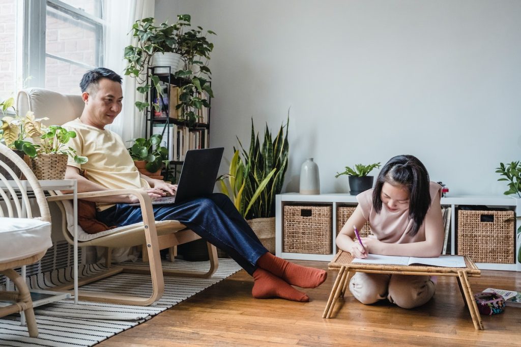 Father looking at her Daughter studying on a Wooden Table