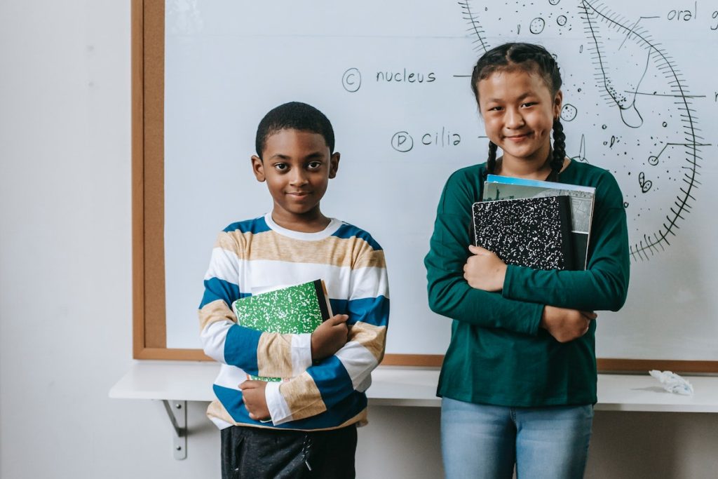 Cheerful multiracial schoolkids with notepads at whiteboard