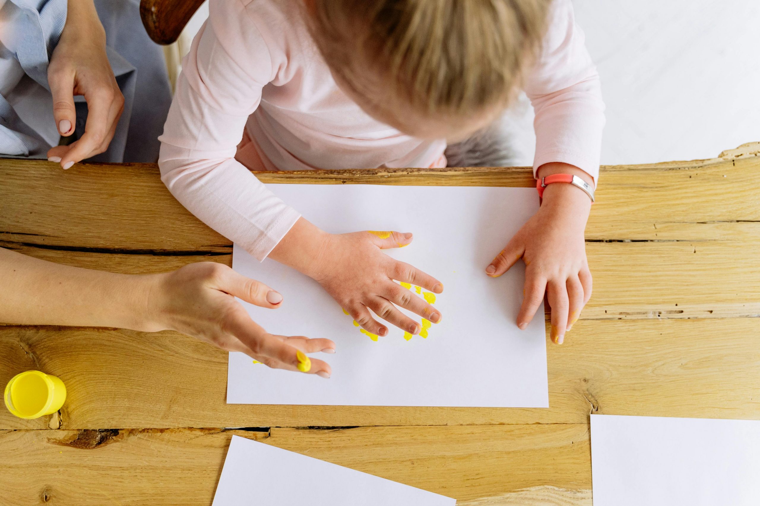 young girl using her finger to spread yellow paint on a sheet of paper